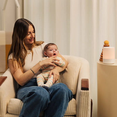 mom smiling and sitting down while holding baby and baby looking at nanit
sound + light