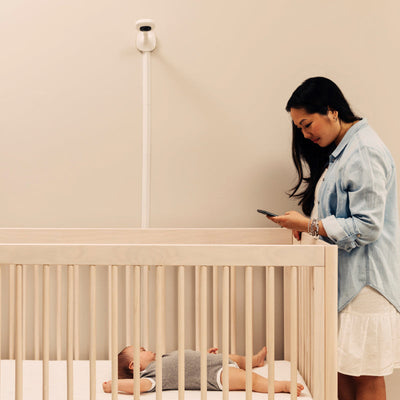 mom looking at phone while watching baby with nanit pro camera + wall mount facing on crib