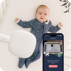 Baby wearing Nanit pajamas with Pro Camera over crib with display of mobile with view to Pro Camera with baby in crib.