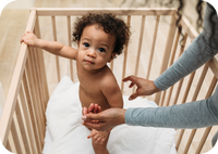 baby in crib with woman reaching out to him