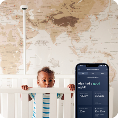 child overlooking over crib with display of nanit app on mobile in foreground with nanit pro camera wall mount in background