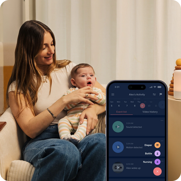 Mom holding baby in Nanit pajamas with  iPhne displayed with baby's activity on APP