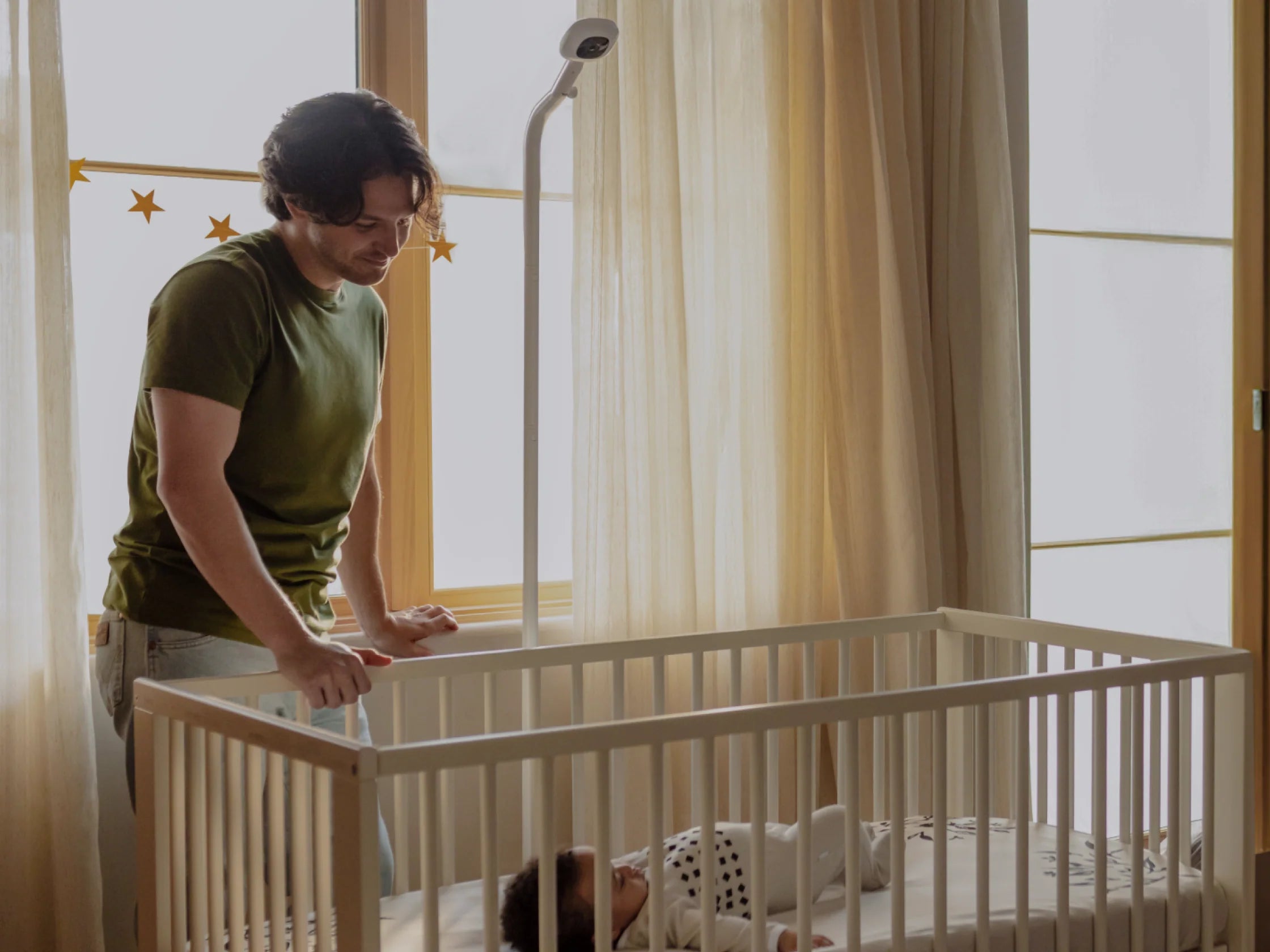 Man looking over at a baby in crib with Pro Camera in background